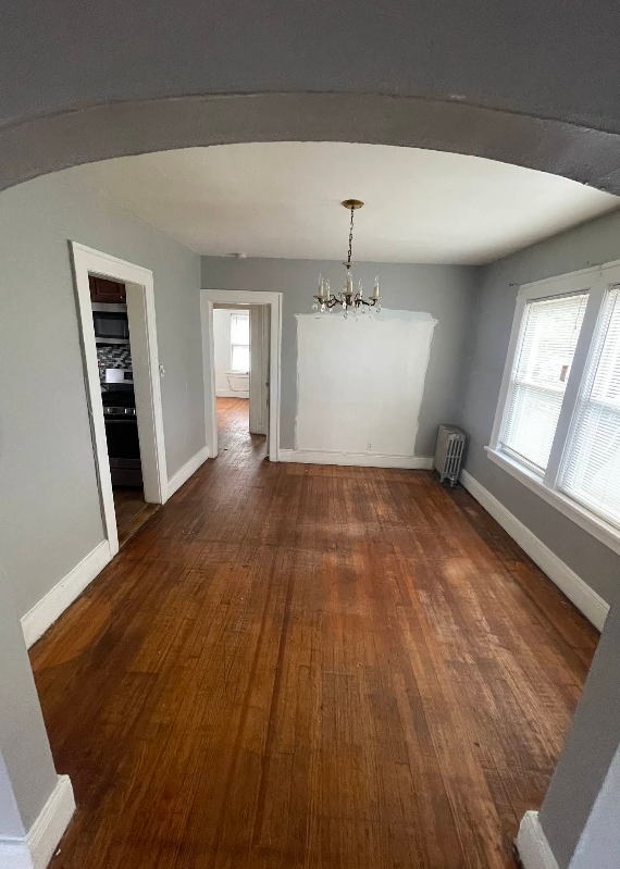 Empty dining room with hardwood floors, gray walls, arched doorway, chandelier, and a white, built-in structure.