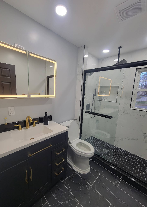 Modern bathroom with black vanity, gold fixtures, and glass shower.
