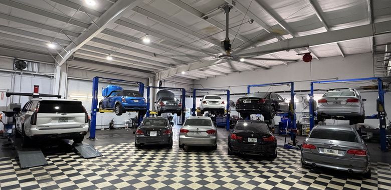 Indoor auto workshop with several parked cars and a blue vehicle on lifts under a high metal ceiling