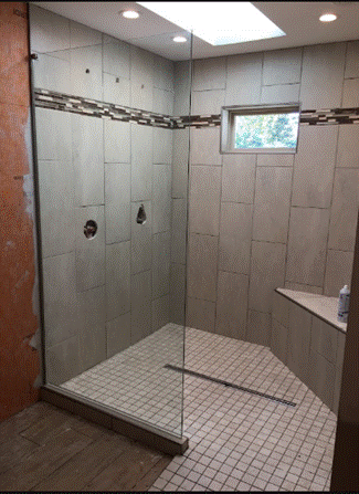 Tiled walk-in shower with glass enclosure, built-in shelf, and window near the ceiling