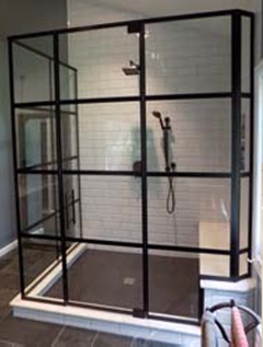 Black-framed walk-in shower with glass panels, white tile walls, and dark floor tiles.