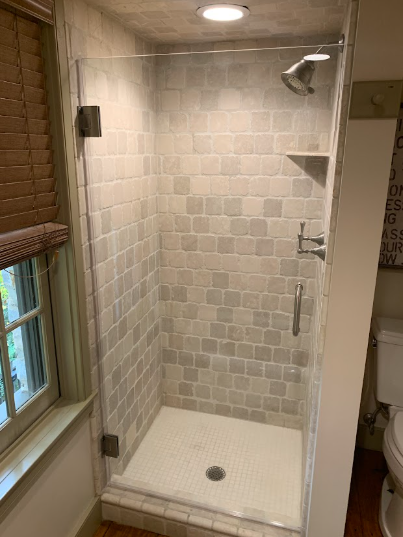 Small tiled walk-in shower with a window, showerhead, and white shower pan in a narrow bathroom.