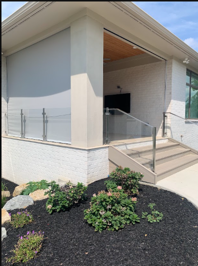 Modern building entrance with steps, ramp railing, and landscaped shrubs in front