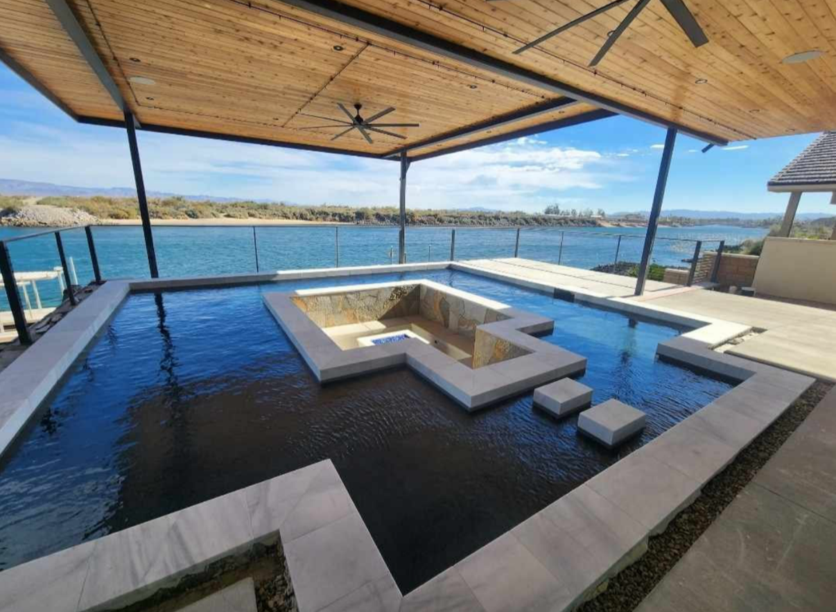 Pool with a unique design, overlooking a tranquil blue sea under a shaded structure.