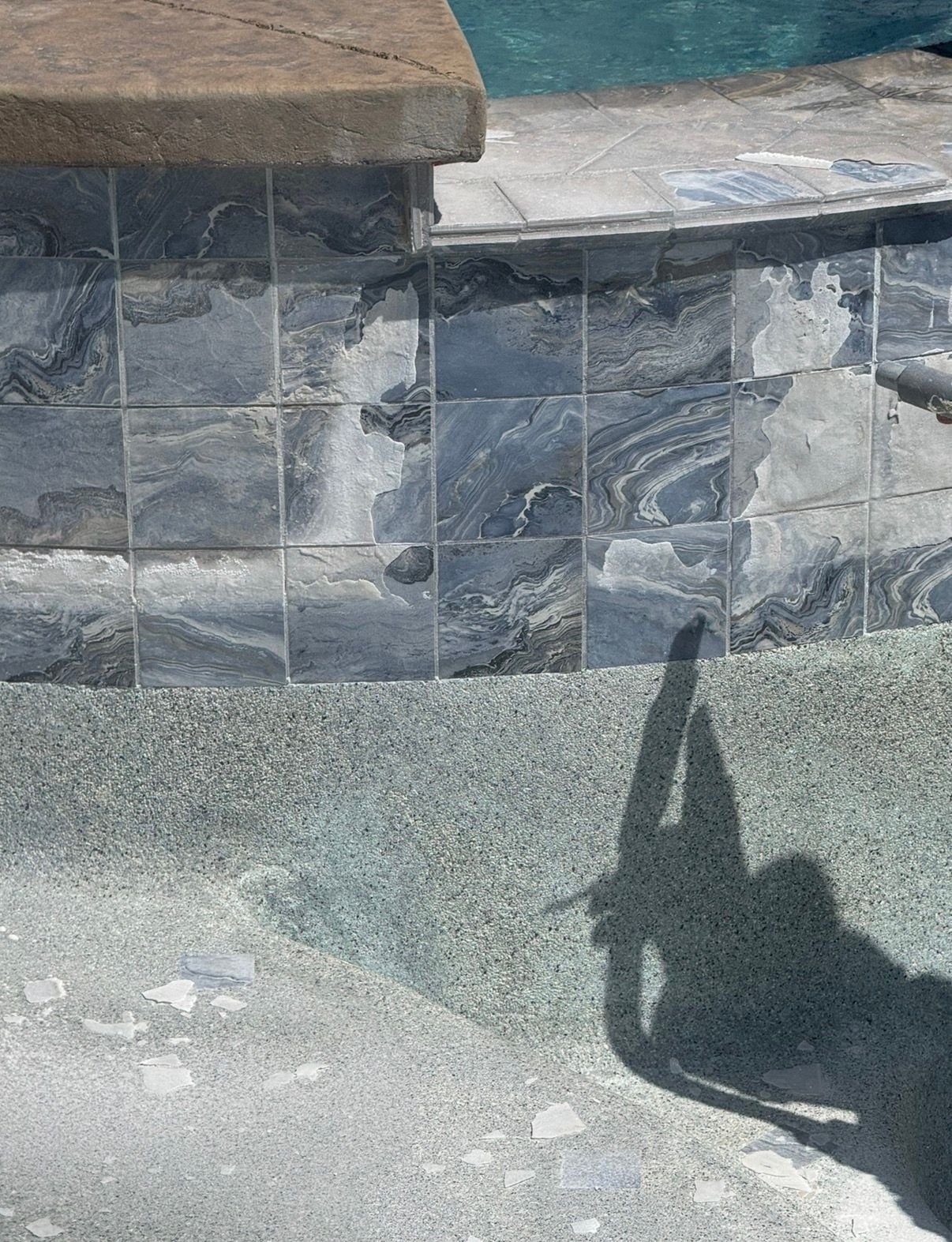 Close-up of a pool's tile and coping. Shadow of a person falls on the pool's textured surface.