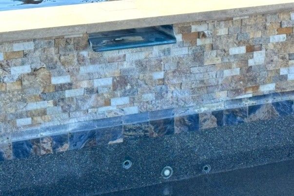 Stone pool wall with waterline tiles, an outlet, and pool jets.