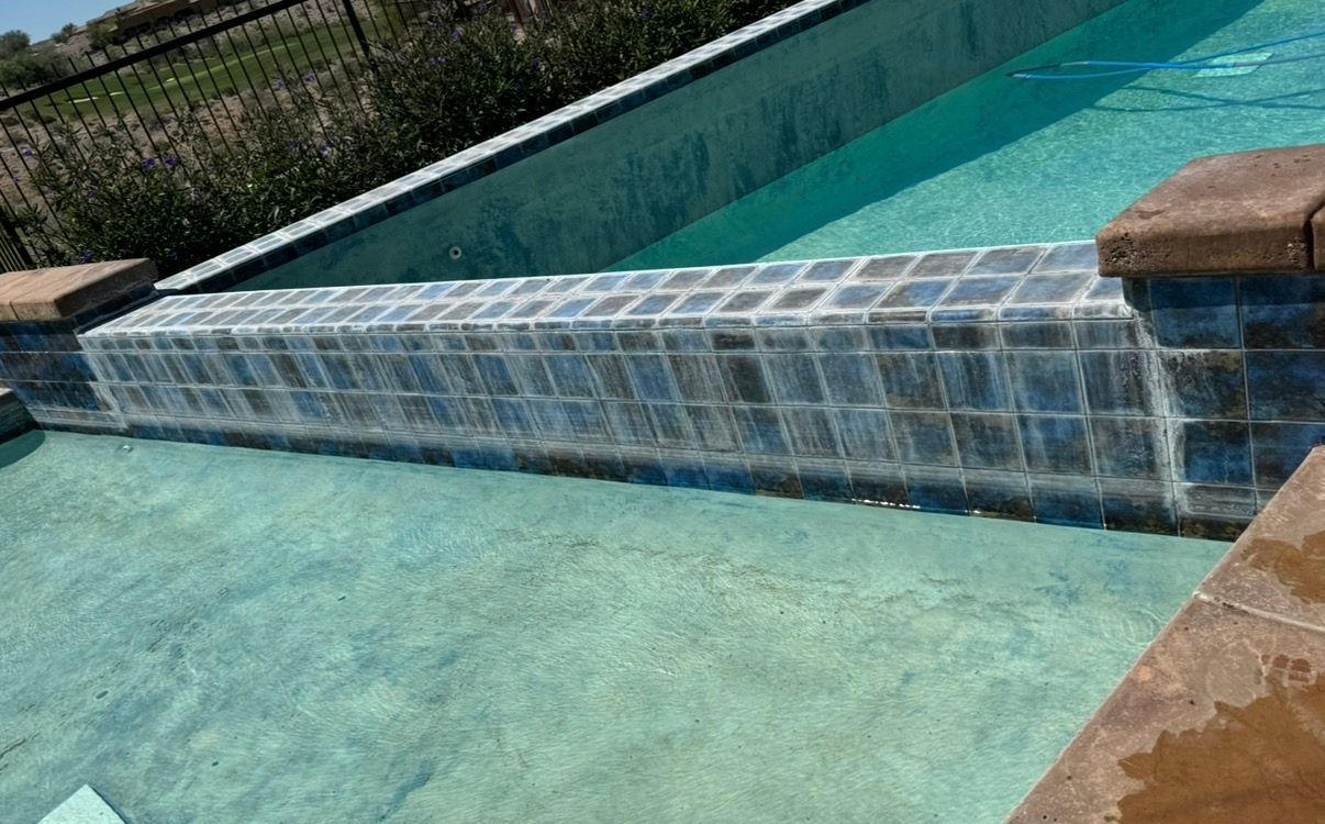 Pool with cascading water feature, blue tiles, turquoise water, brown coping.