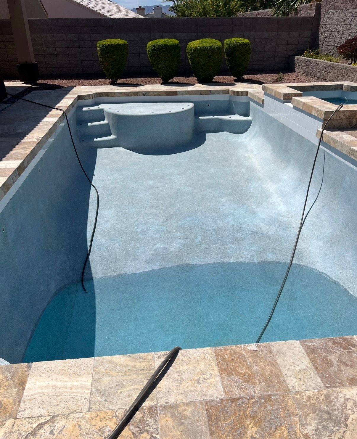 Empty light blue pool with travertine coping and a circular raised area, set outdoors.