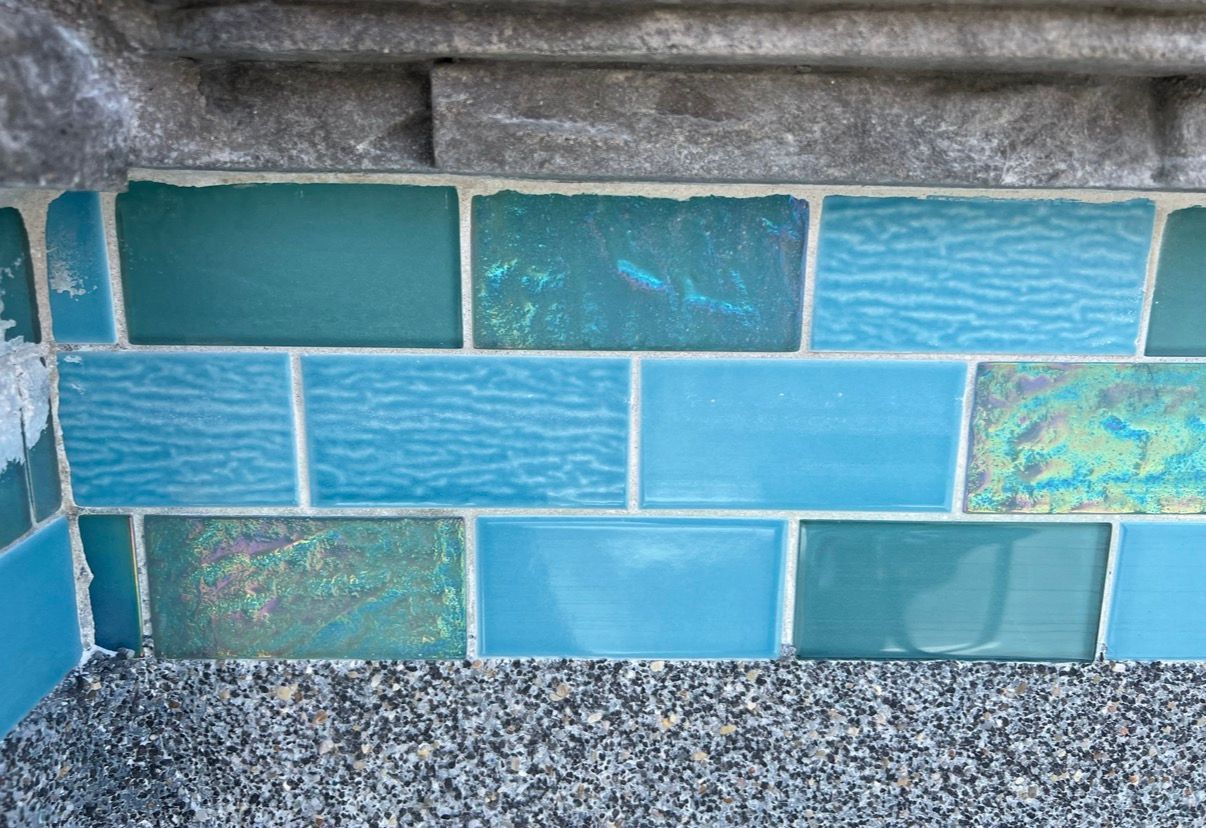 Blue and turquoise tiled wall with white grout, next to a stone border.