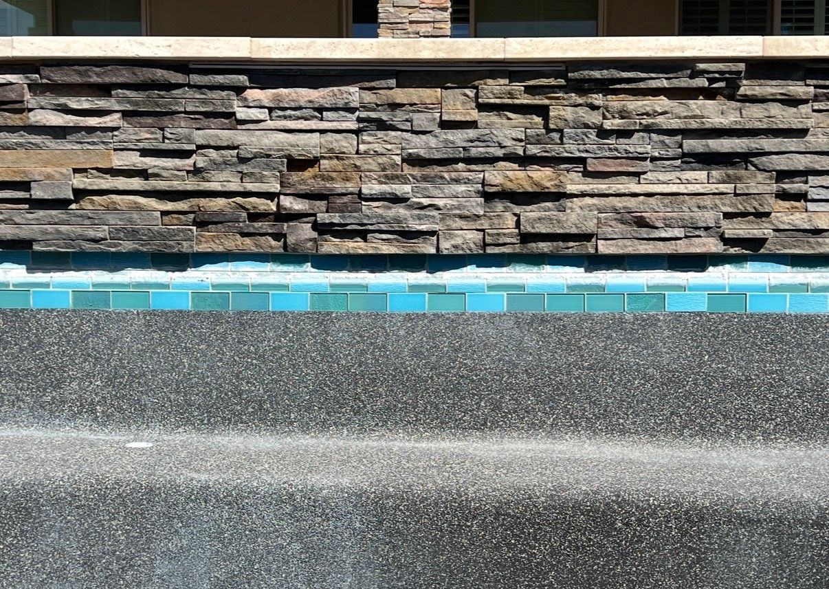 Pool with stone wall, teal waterline tile, and dark textured surface.