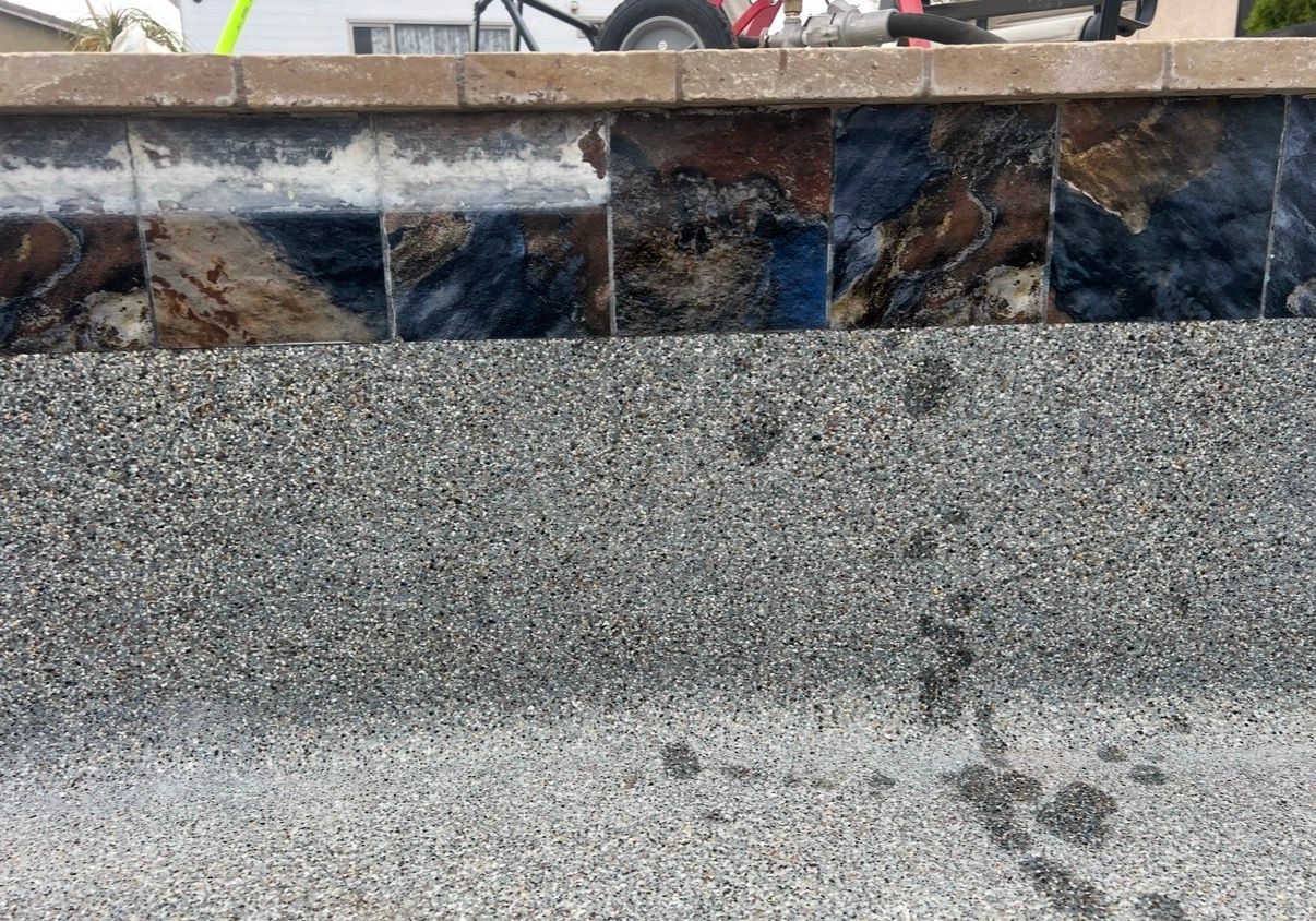 Pool wall with dark marble tiles and gray pebble finish.