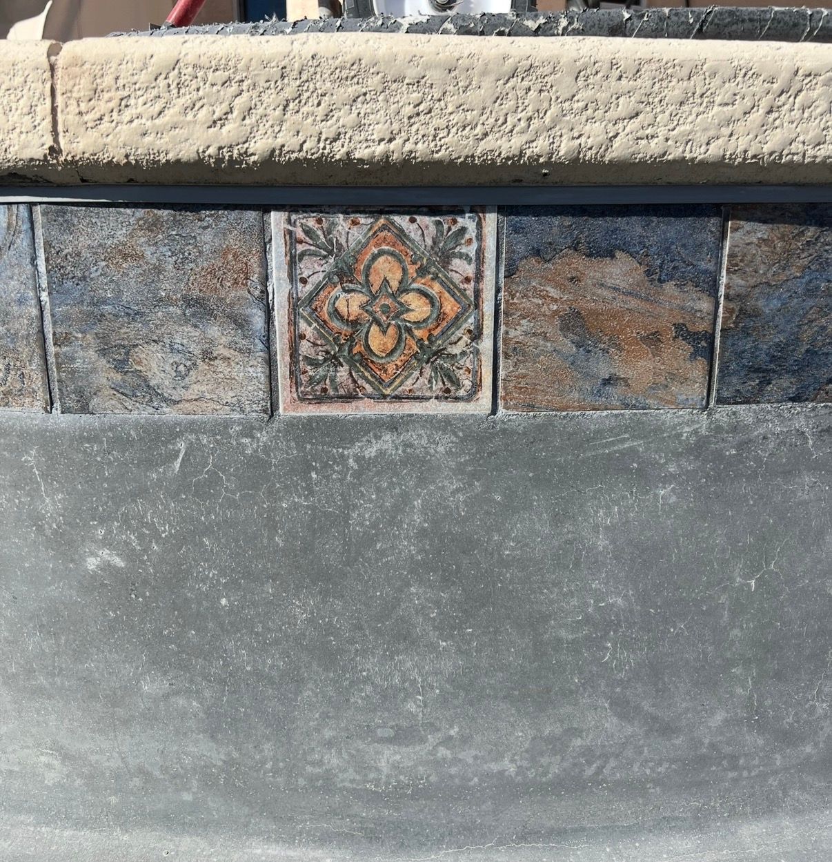 Close-up of a pool's tile border featuring a decorative flower tile and mottled blue and brown tiles.