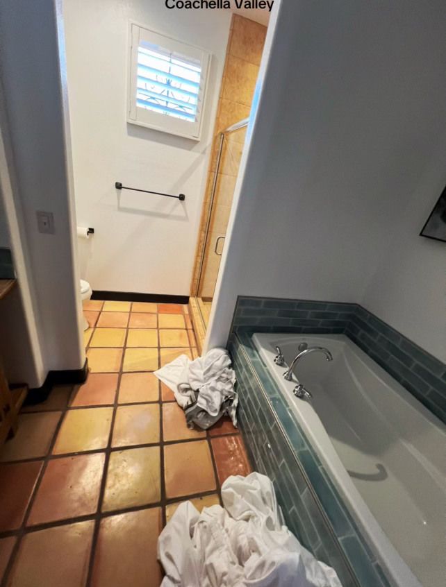 Image of a messy bathroom with clothing all around the floor. 