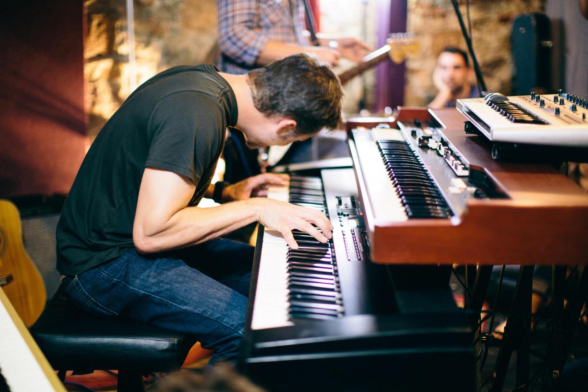A man is sitting on a stool playing a piano.