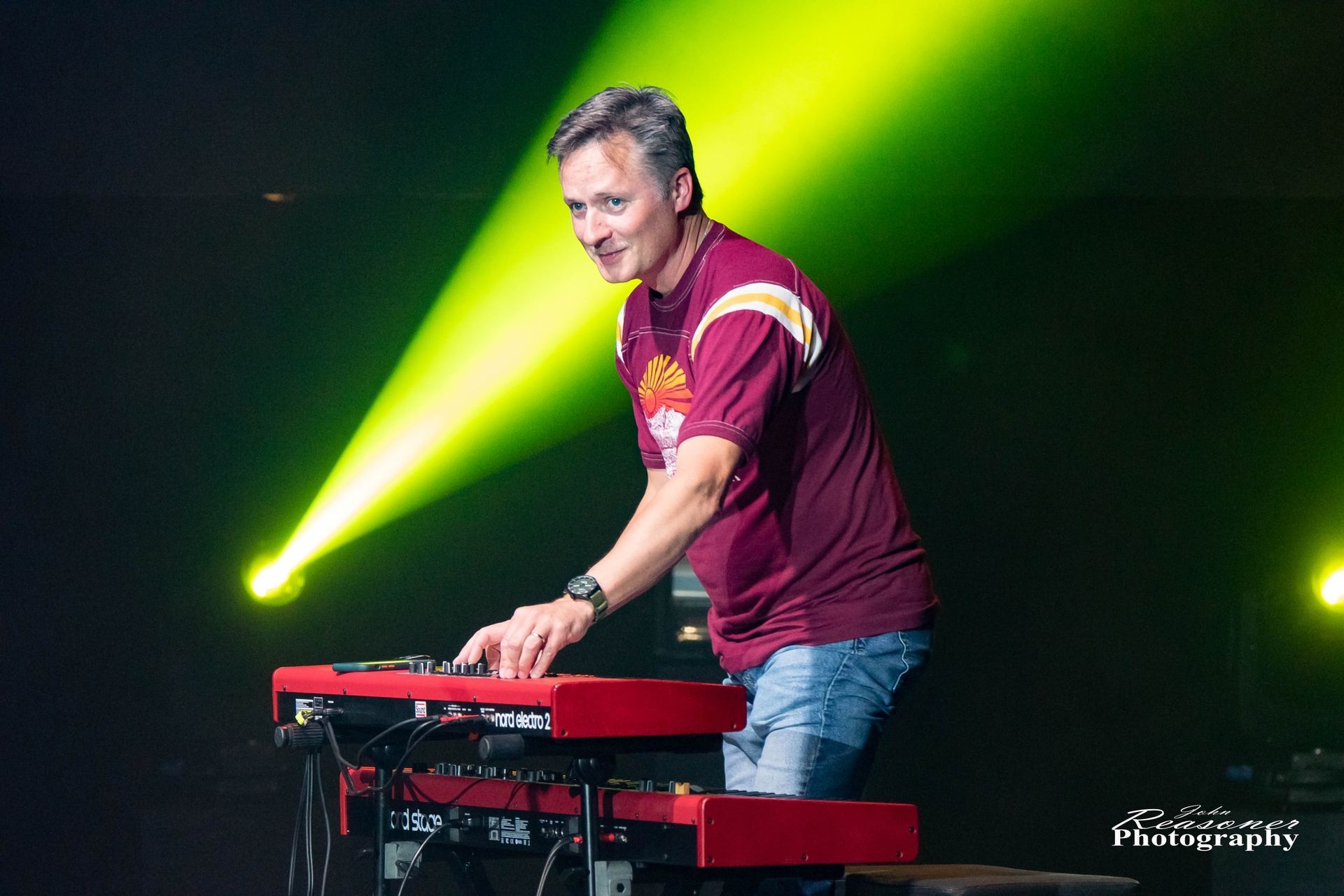 A man in a maroon shirt is playing a keyboard on a stage.
