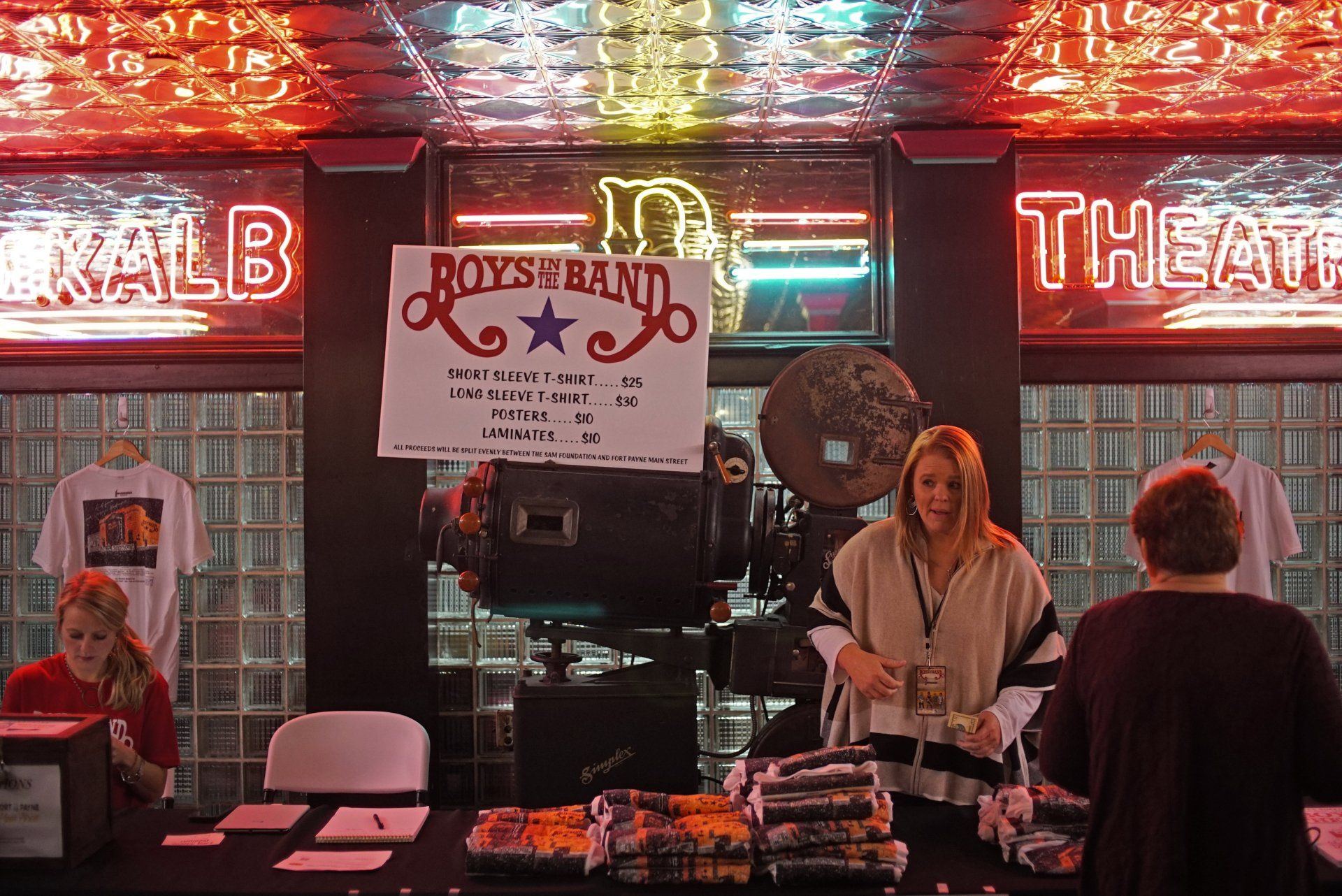 A woman stands behind a table in front of a sign that says rocks band