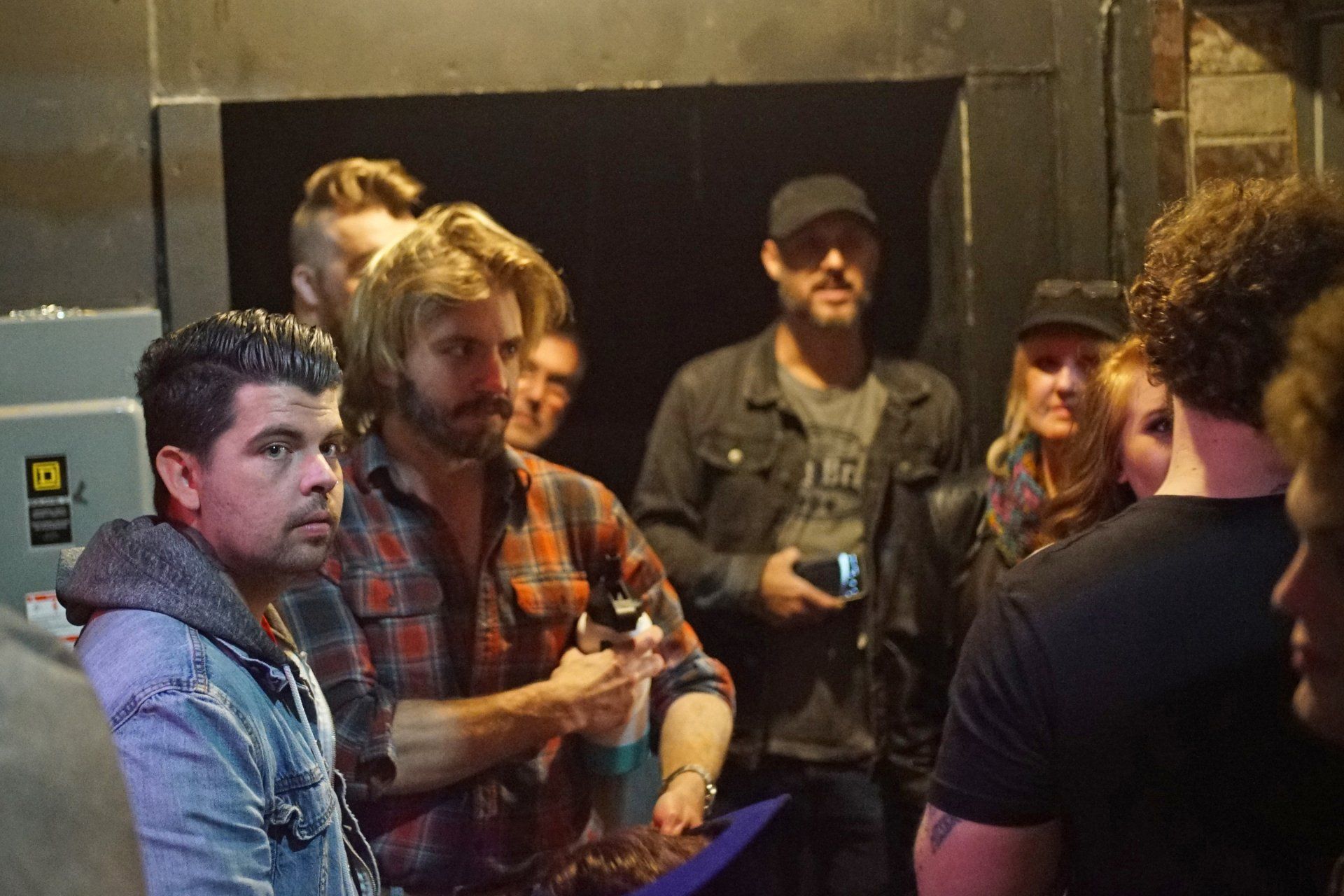A group of people are standing in a dark room talking to each other.