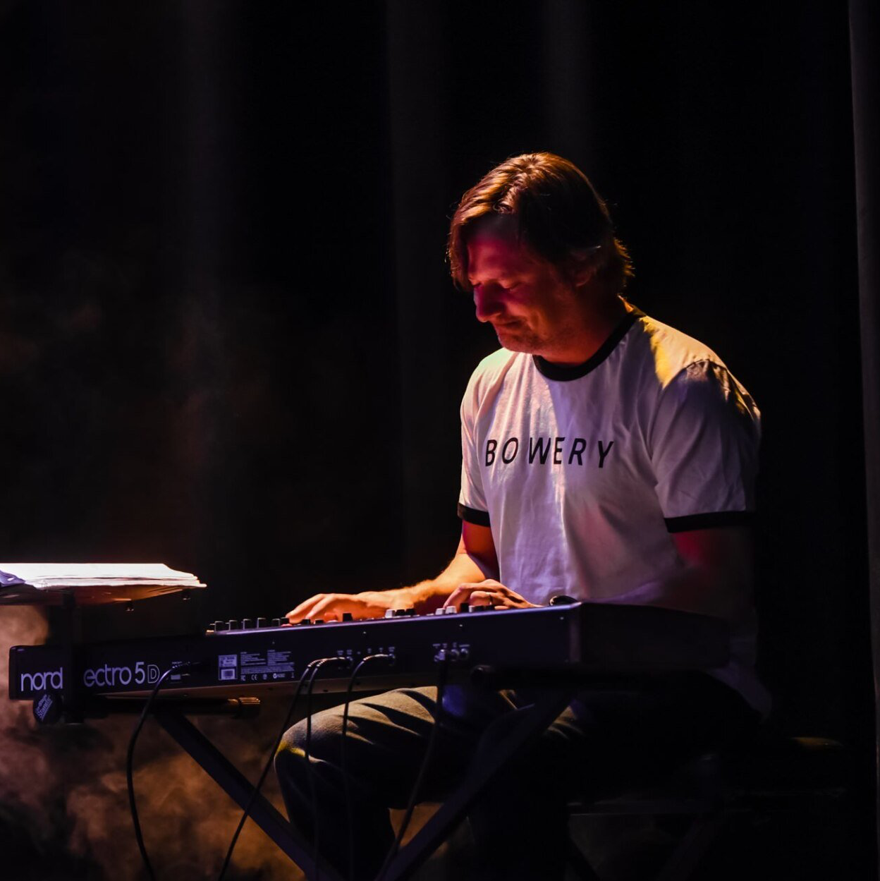 A man in a white shirt that says powery is playing a keyboard