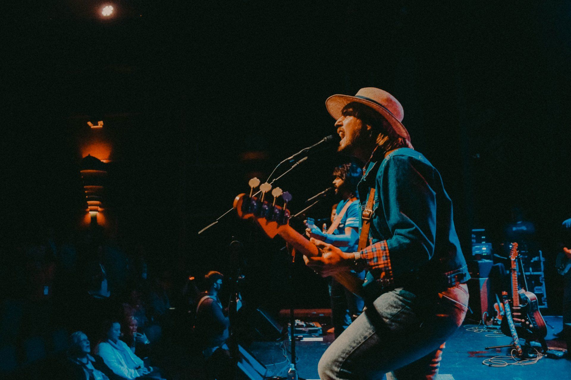 A man in a cowboy hat is singing into a microphone while playing a guitar