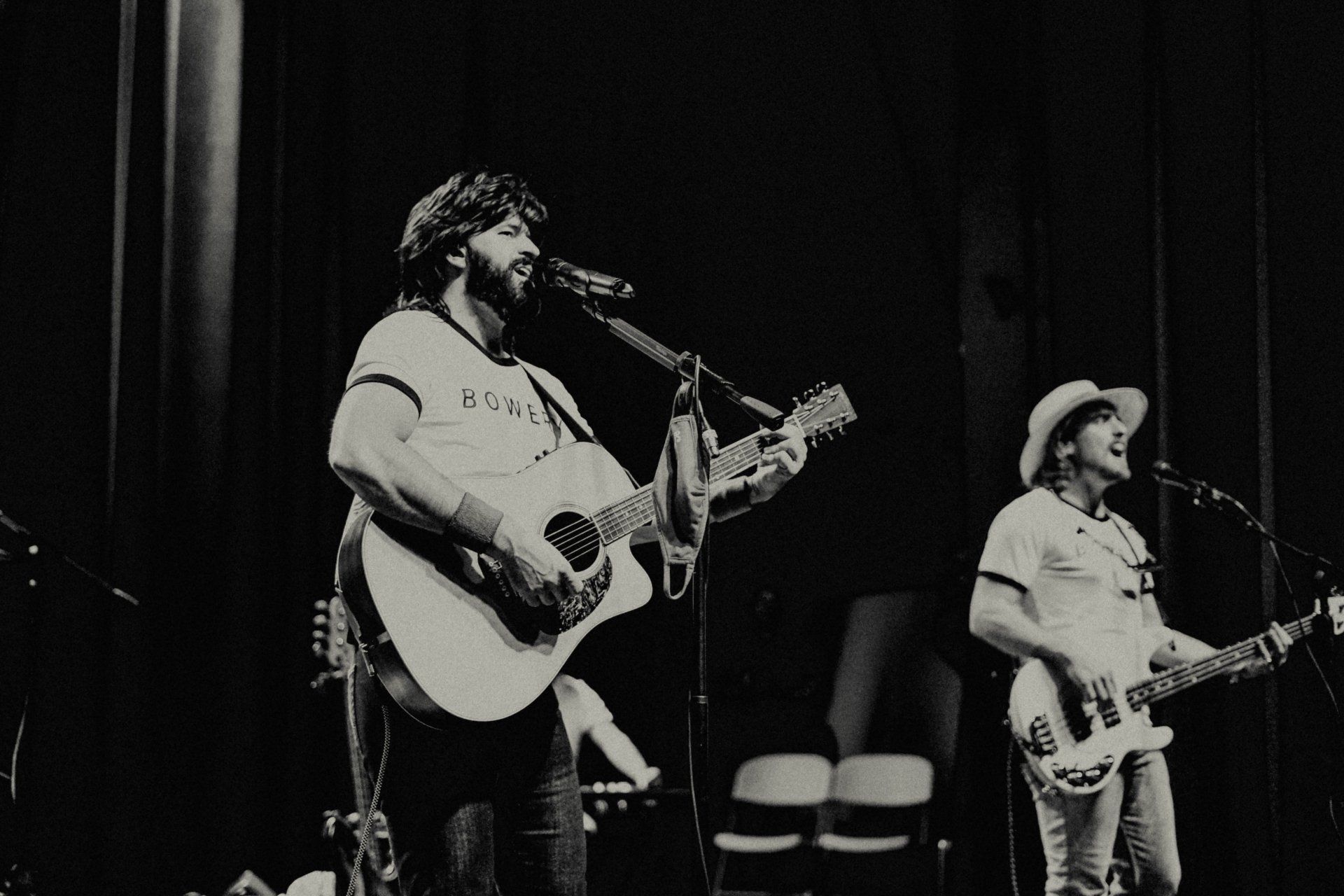 Two men playing guitars and singing into microphones on a stage