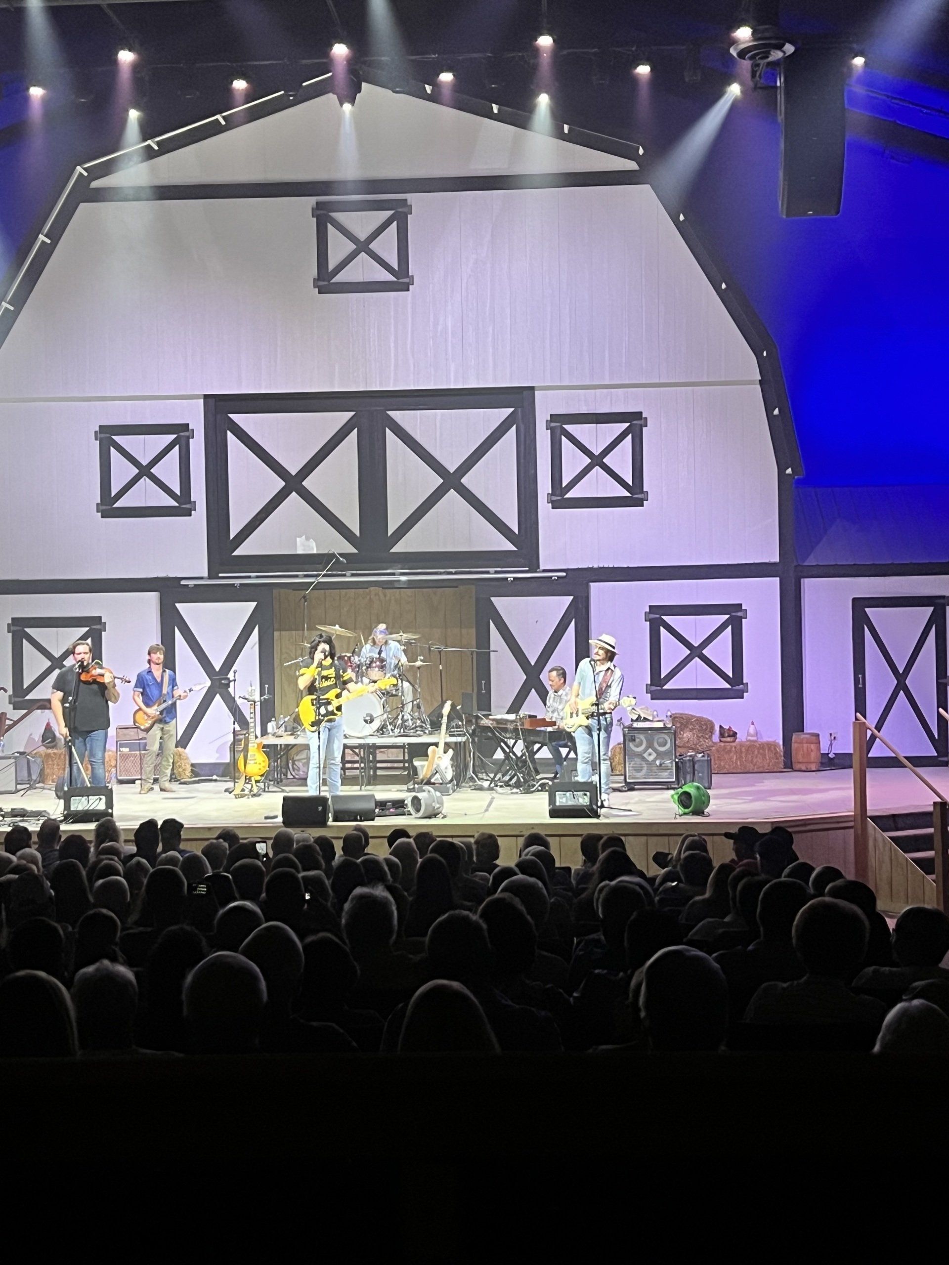 A group of people are playing instruments on a stage in front of a barn.