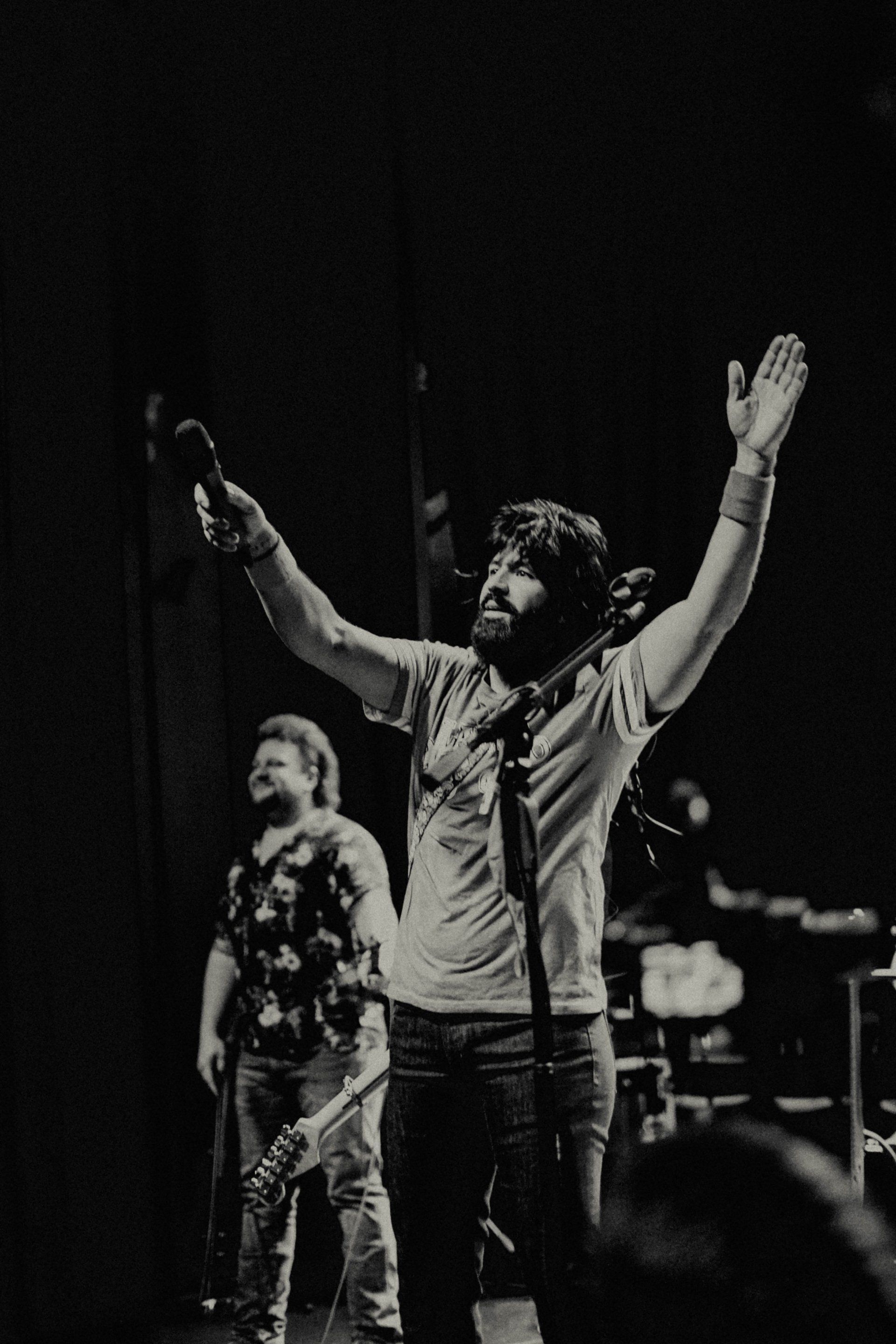 A black and white photo of a man singing into a microphone on a stage.