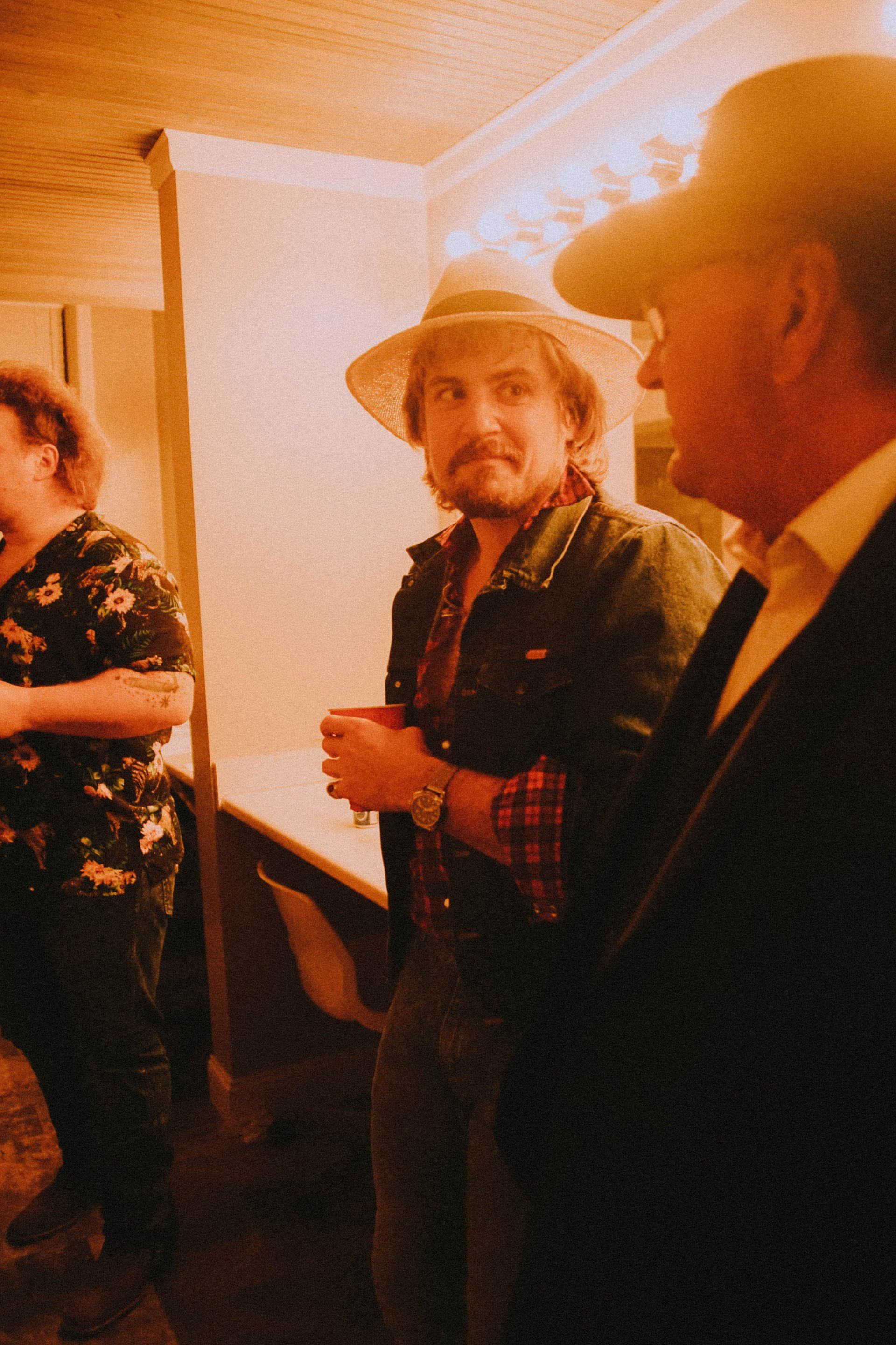 A man in a cowboy hat is standing next to another man in a suit.