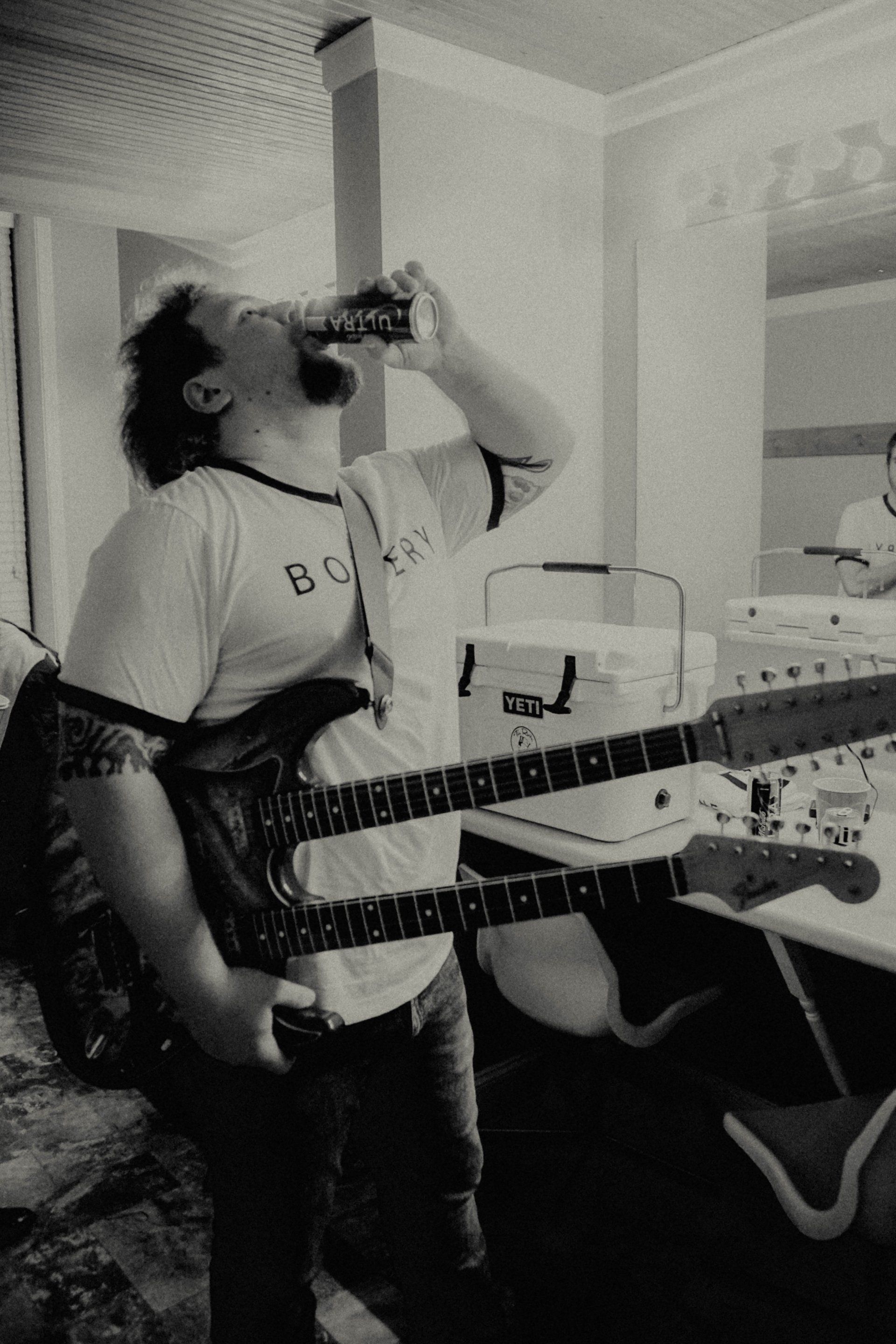 A man drinking from a bottle while holding a guitar