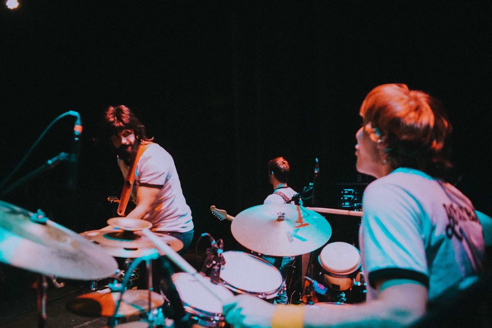 Two men are playing drums on a stage in a dark room