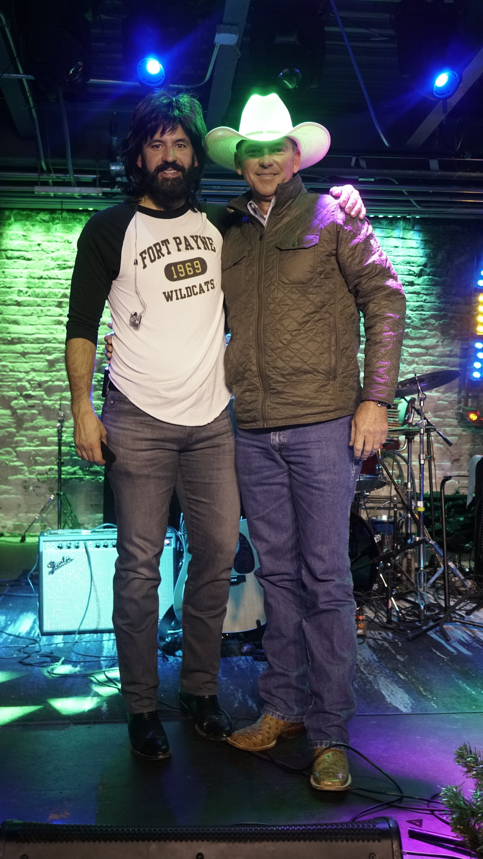 Two men are standing next to each other on a stage . one of the men is wearing a cowboy hat.