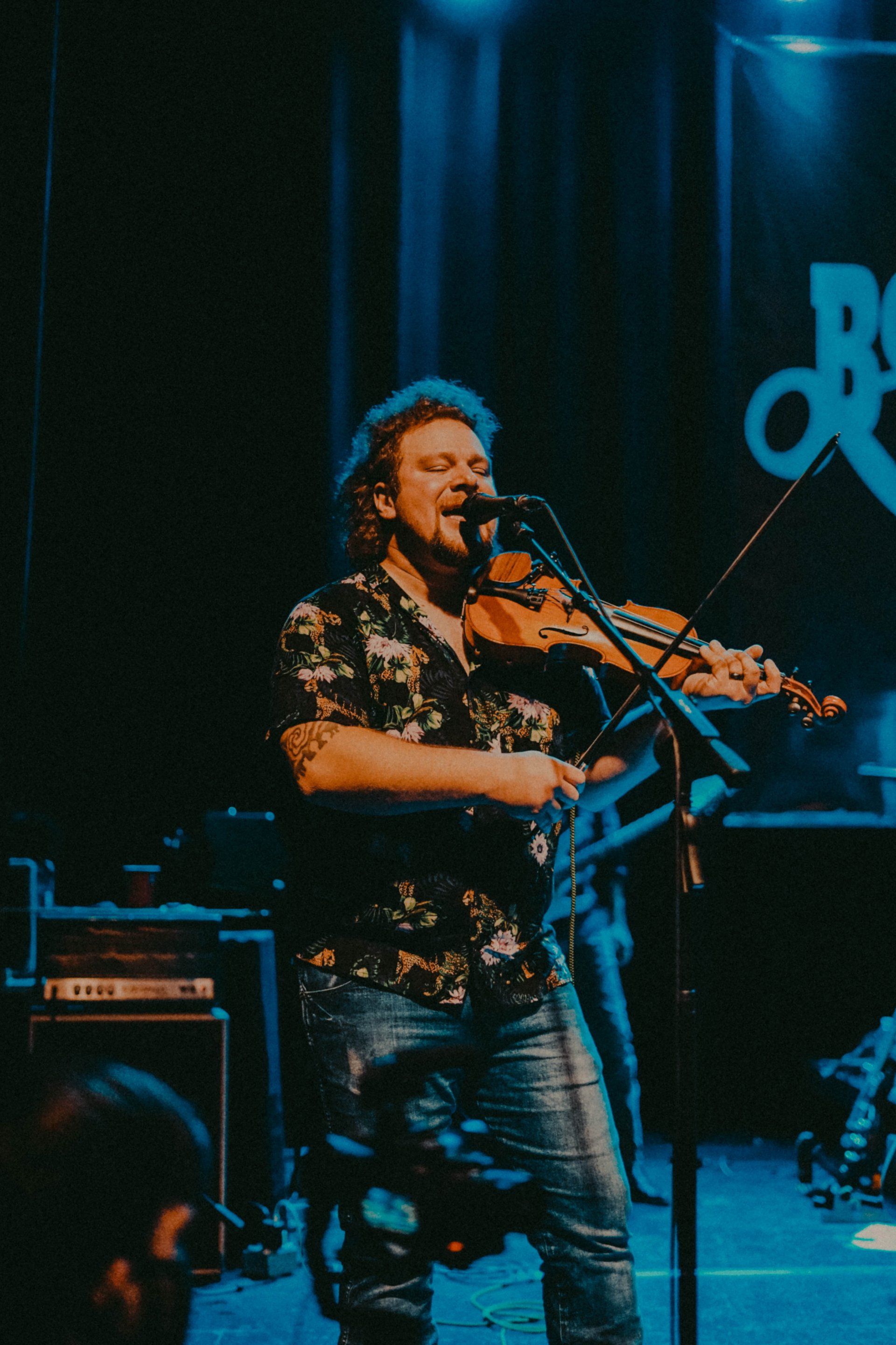 A man is playing a violin and singing into a microphone on a stage.