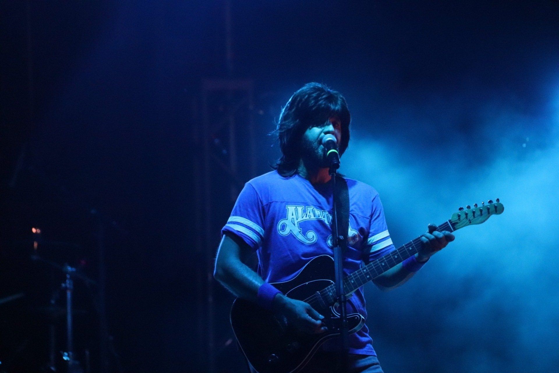 A man in a blue shirt is playing a guitar and singing into a microphone.