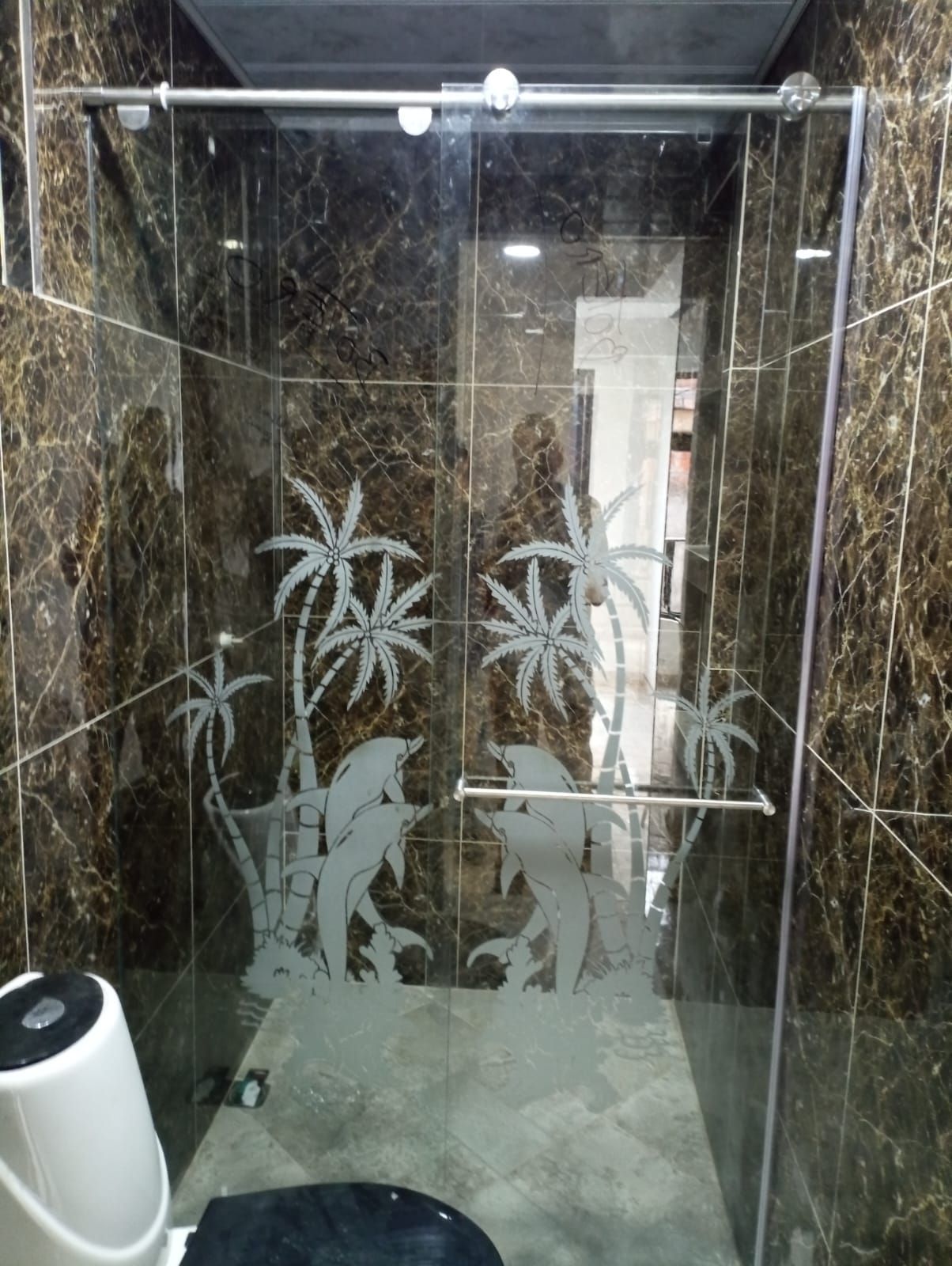 Un baño con una puerta de ducha corrediza de vidrio con un delfín y palmeras en ella.