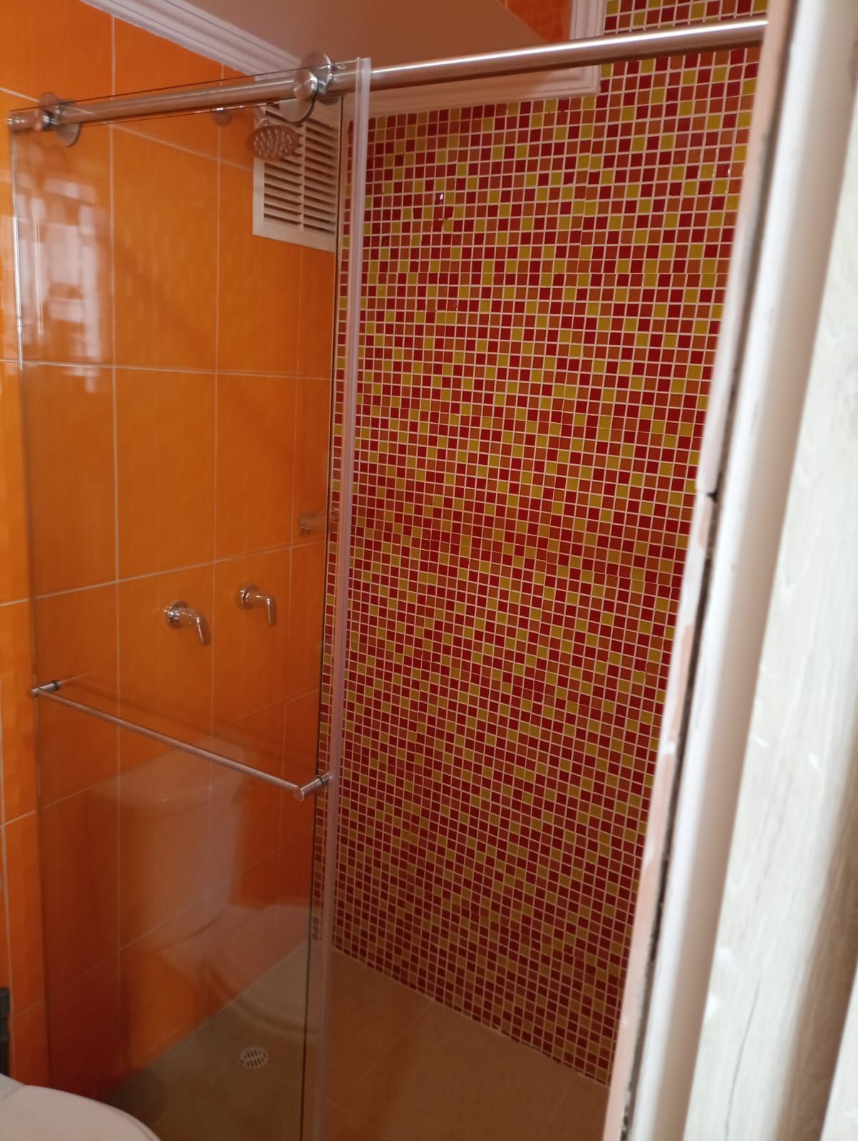 Un baño con azulejos naranjas y una puerta de ducha de cristal.