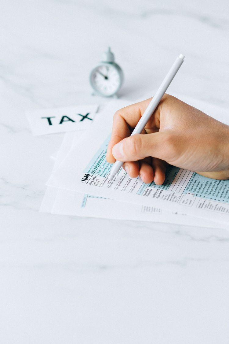Hand writing on tax form beside a clock on a white desk