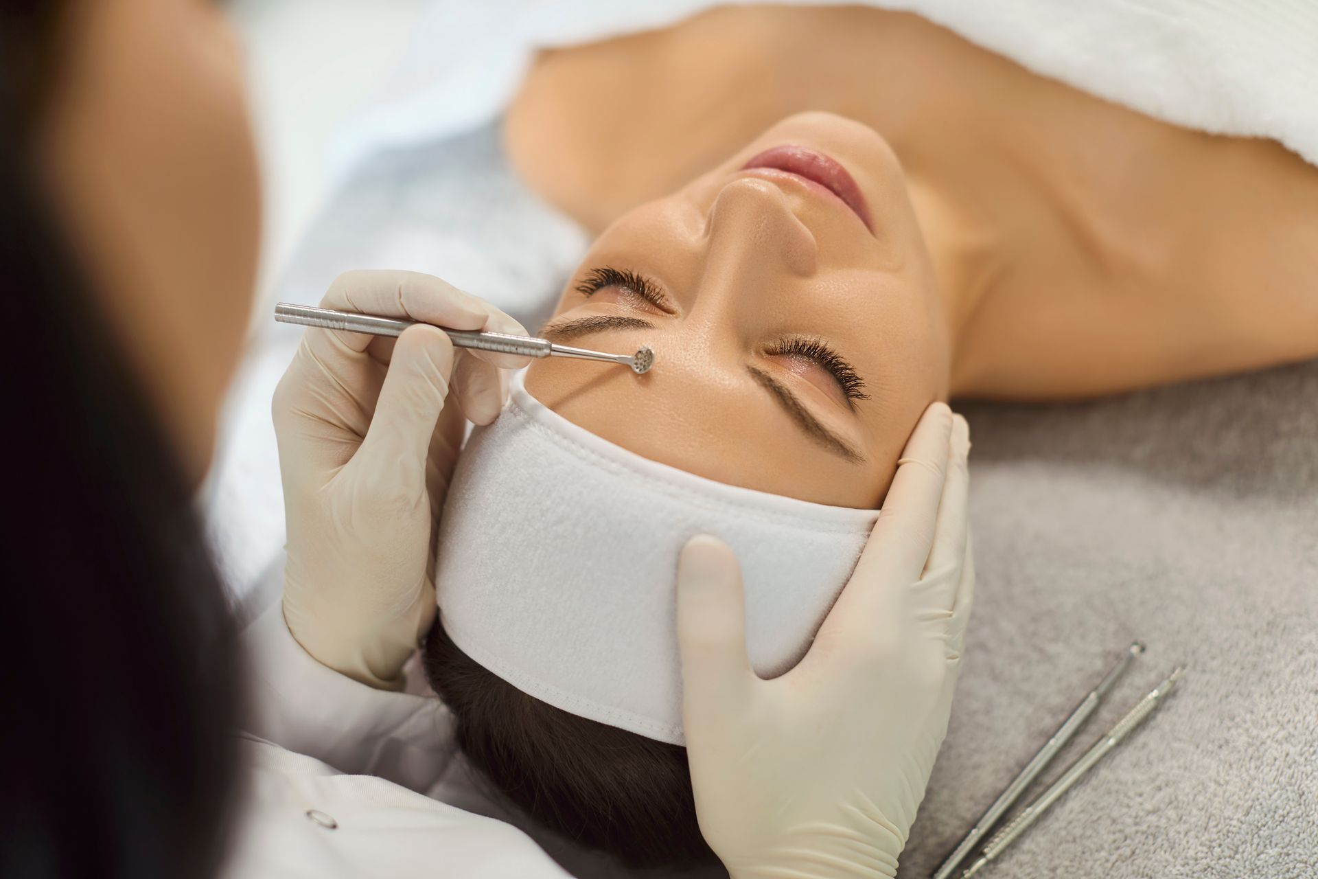 Cosmetic procedure on a woman’s face with a practitioner using gloved hands and a syringe near her lip