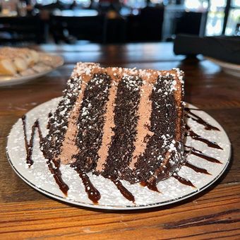 a slice of chocolate cake on a white plate on a wooden table