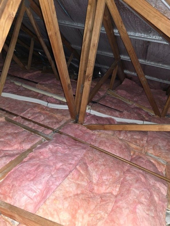 Pink fiberglass insulation around wooden roof trusses in an attic space