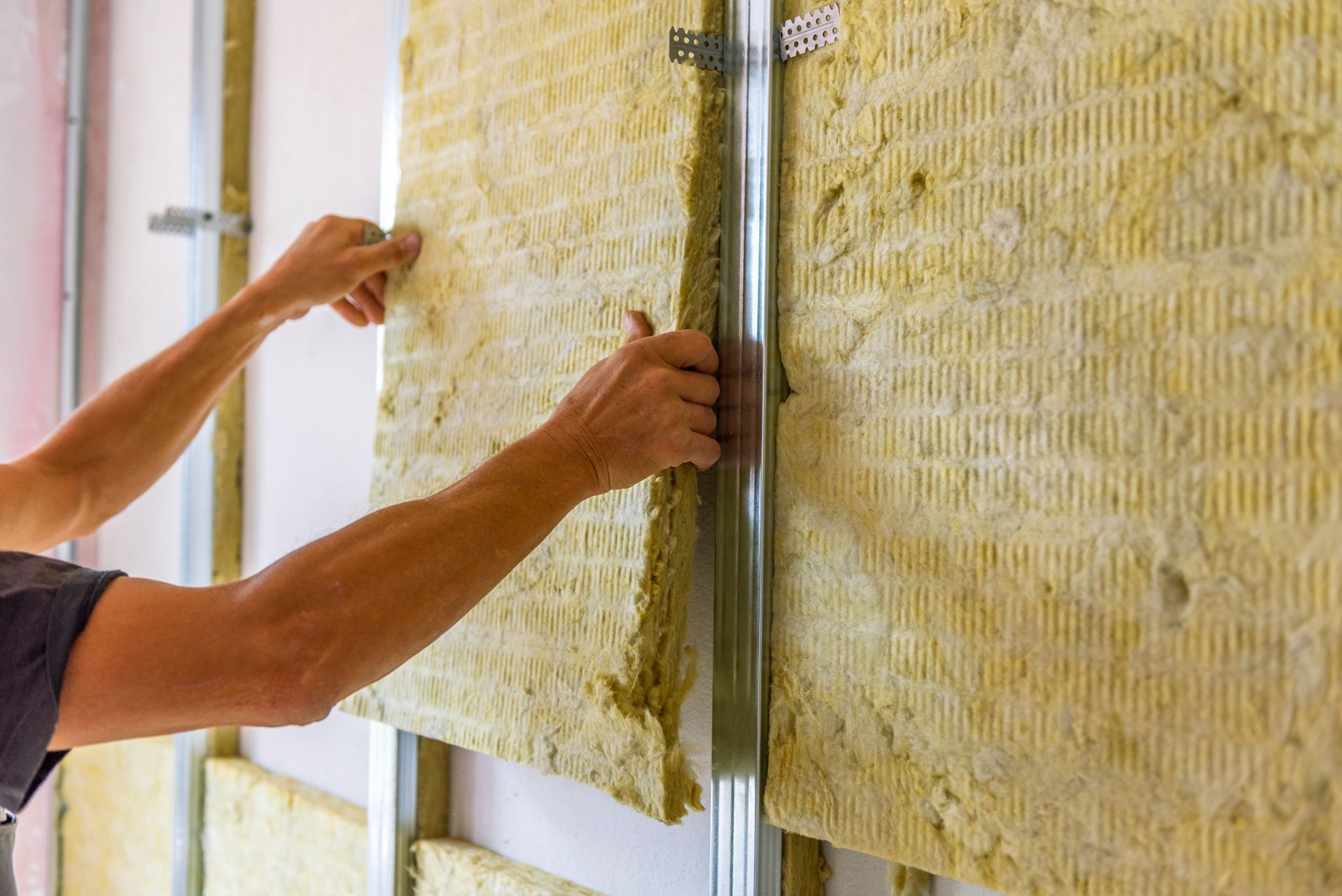 Hands positioning yellow insulation batts between wall studs in a construction frame