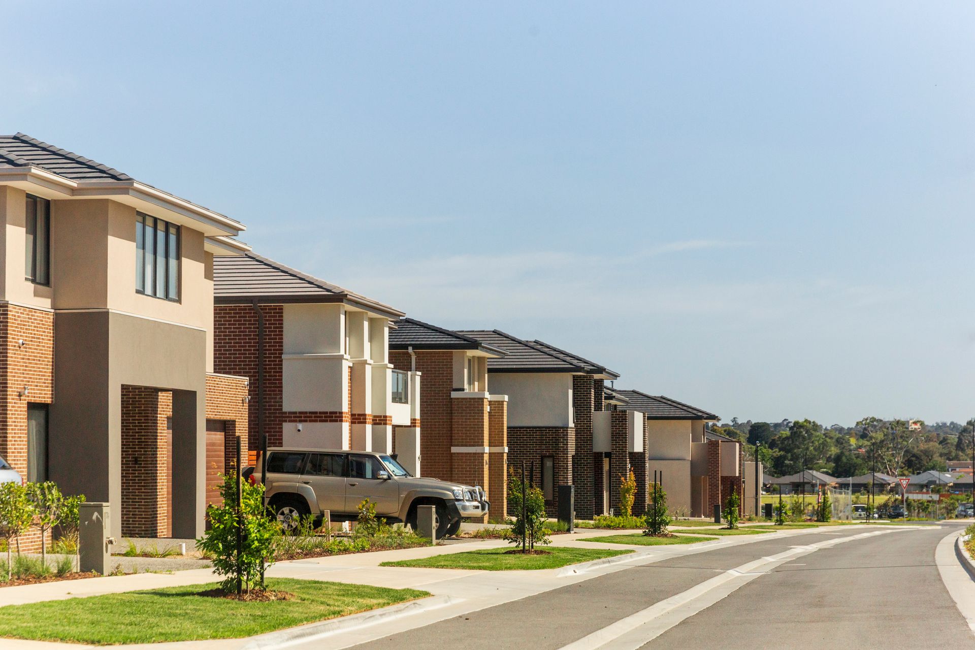 Suburban street with modern houses, parked cars, and a curved road under a clear sky