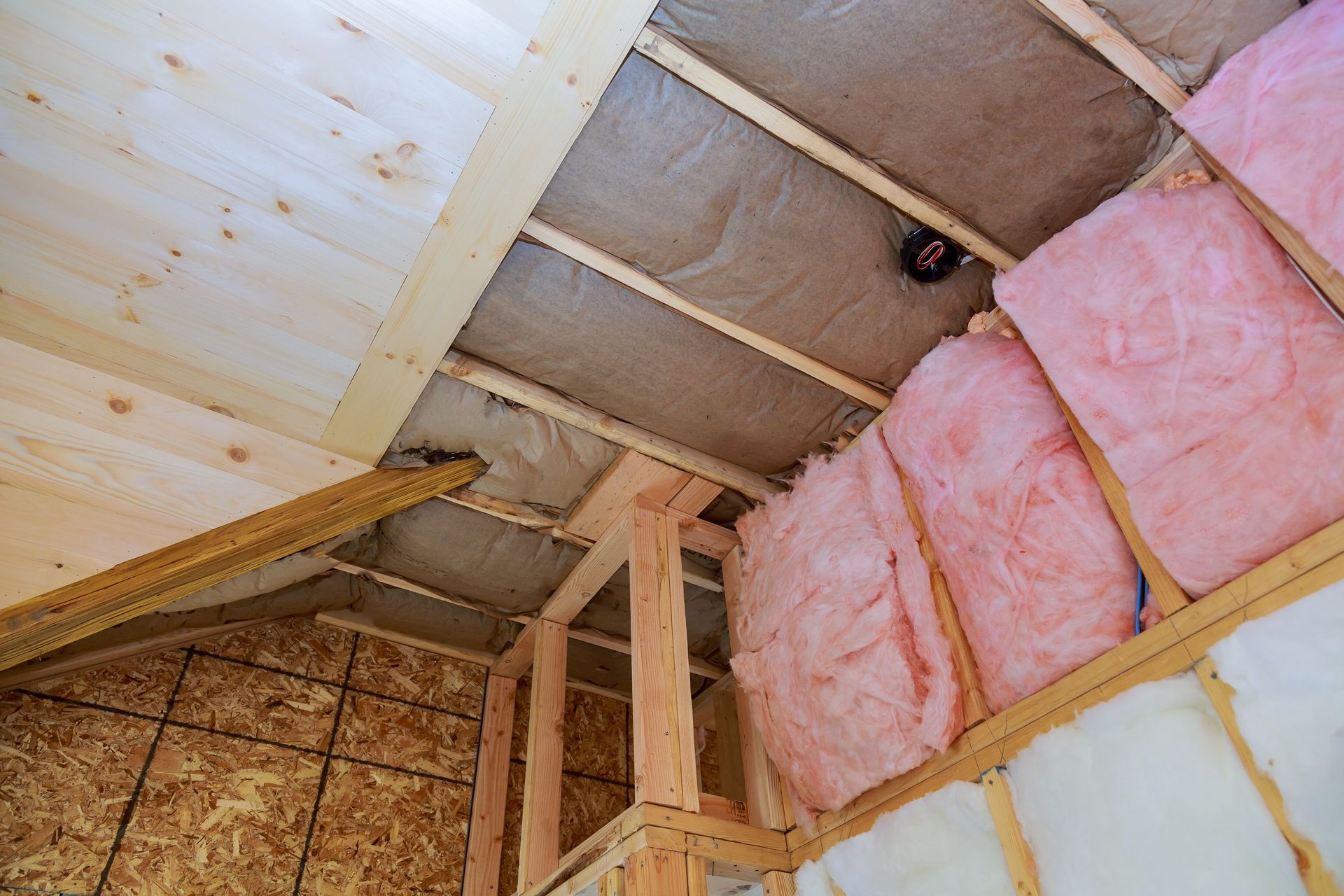 Ceiling insulation under construction with pink fiberglass batts and exposed wooden rafters