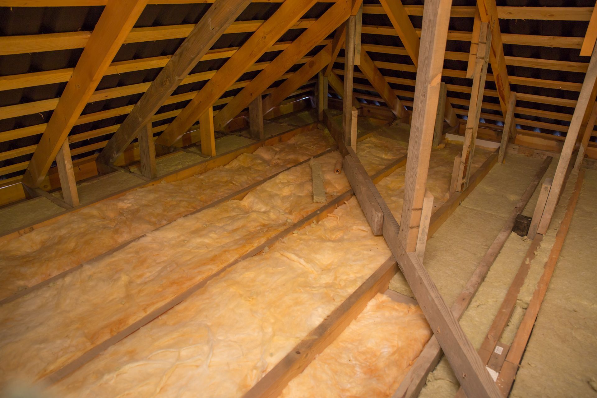 Attic with wooden roof trusses and exposed insulation under the rafters.