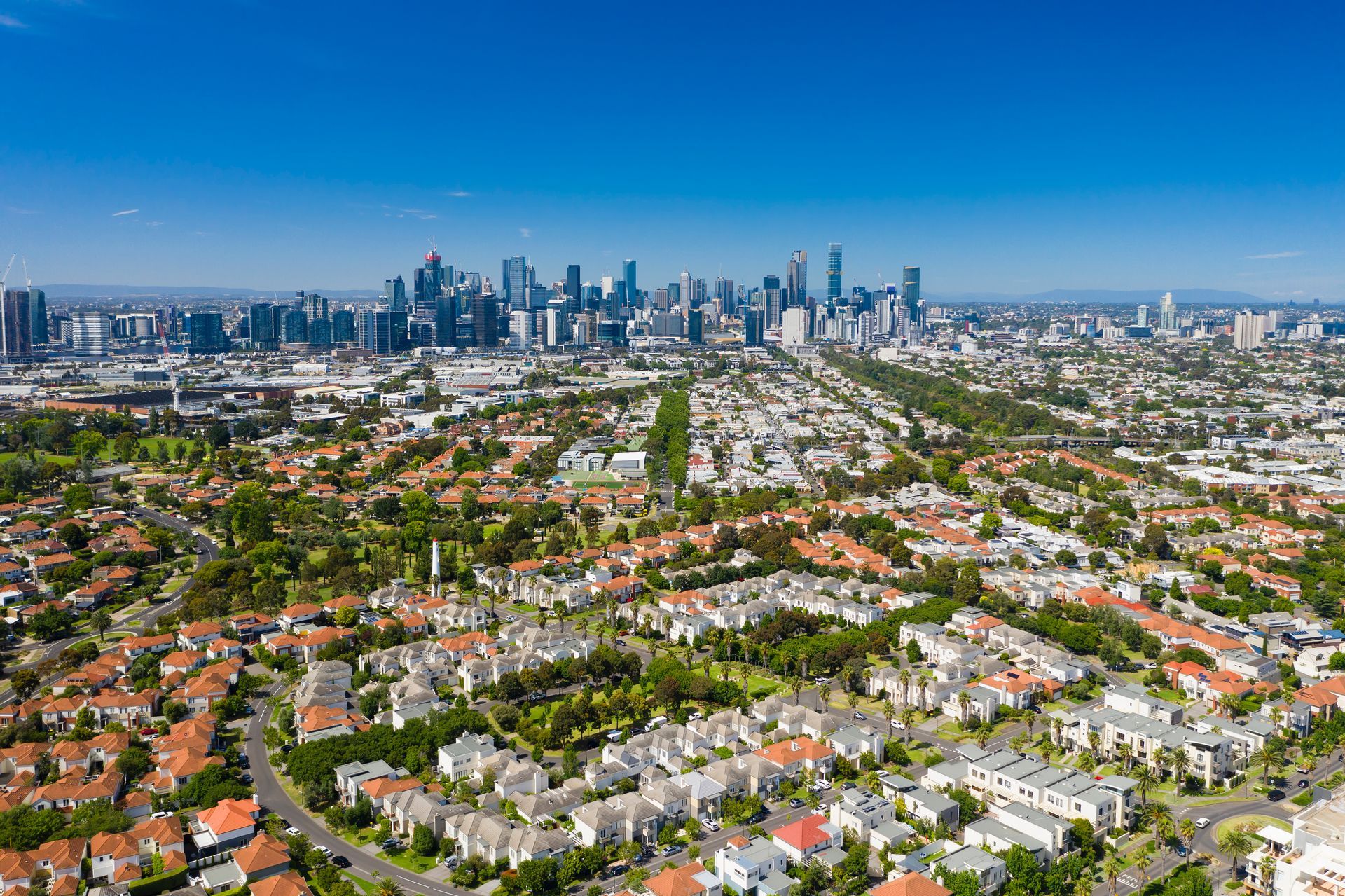 Aerial view of a suburban neighborhood leading to a distant city skyline under a clear blue sky