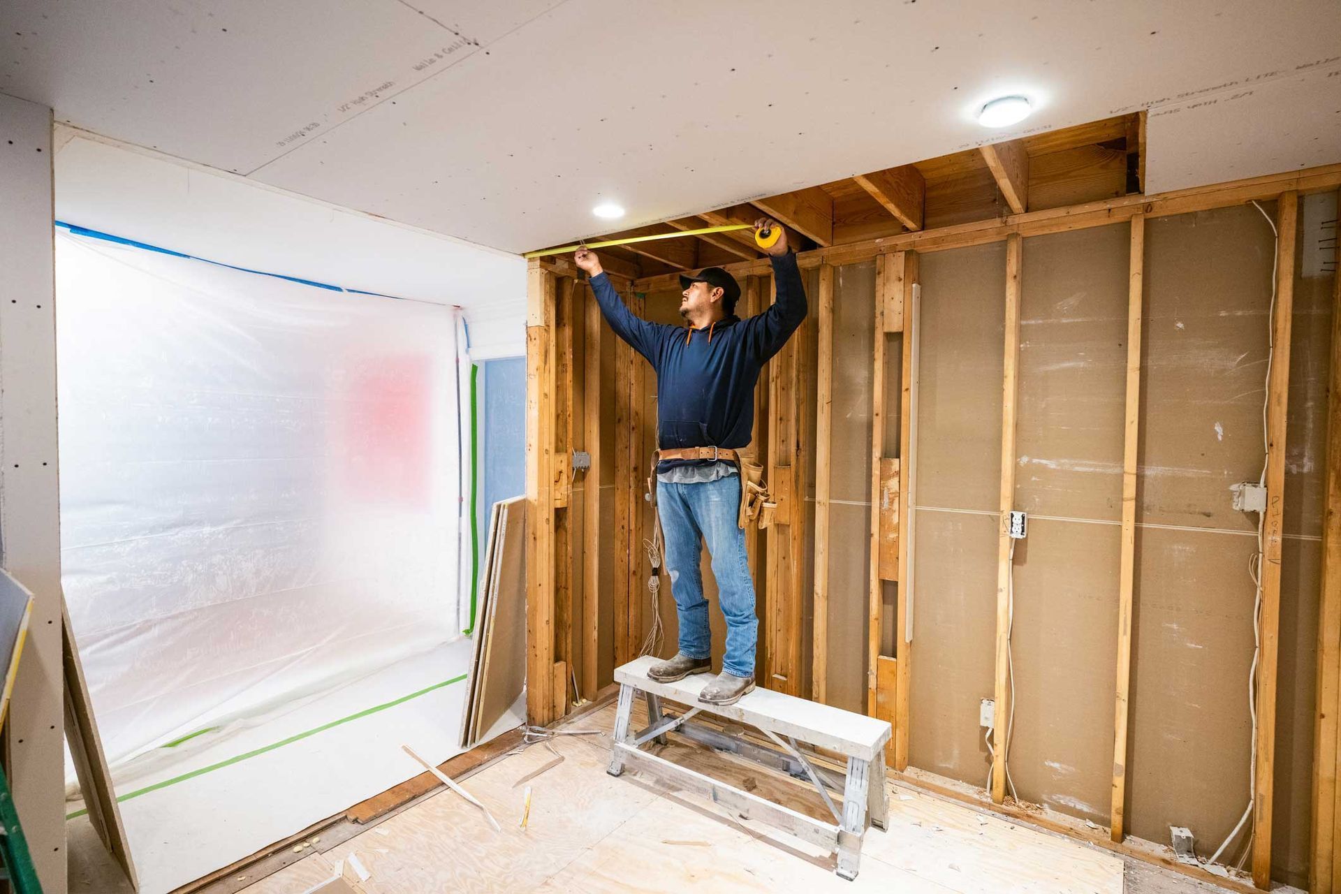 Worker standing on a step ladder framing an unfinished interior wall during home renovation