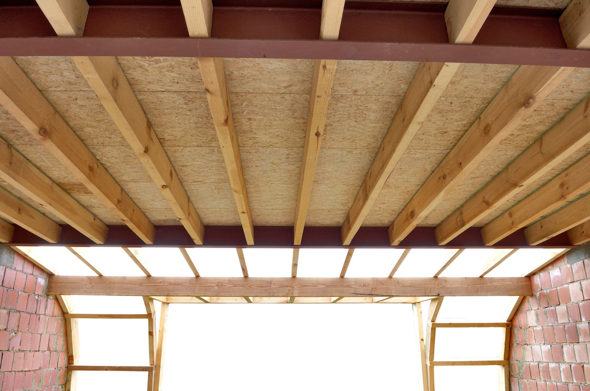 Unfinished roof interior with exposed wooden beams and brick side walls around a bright opening