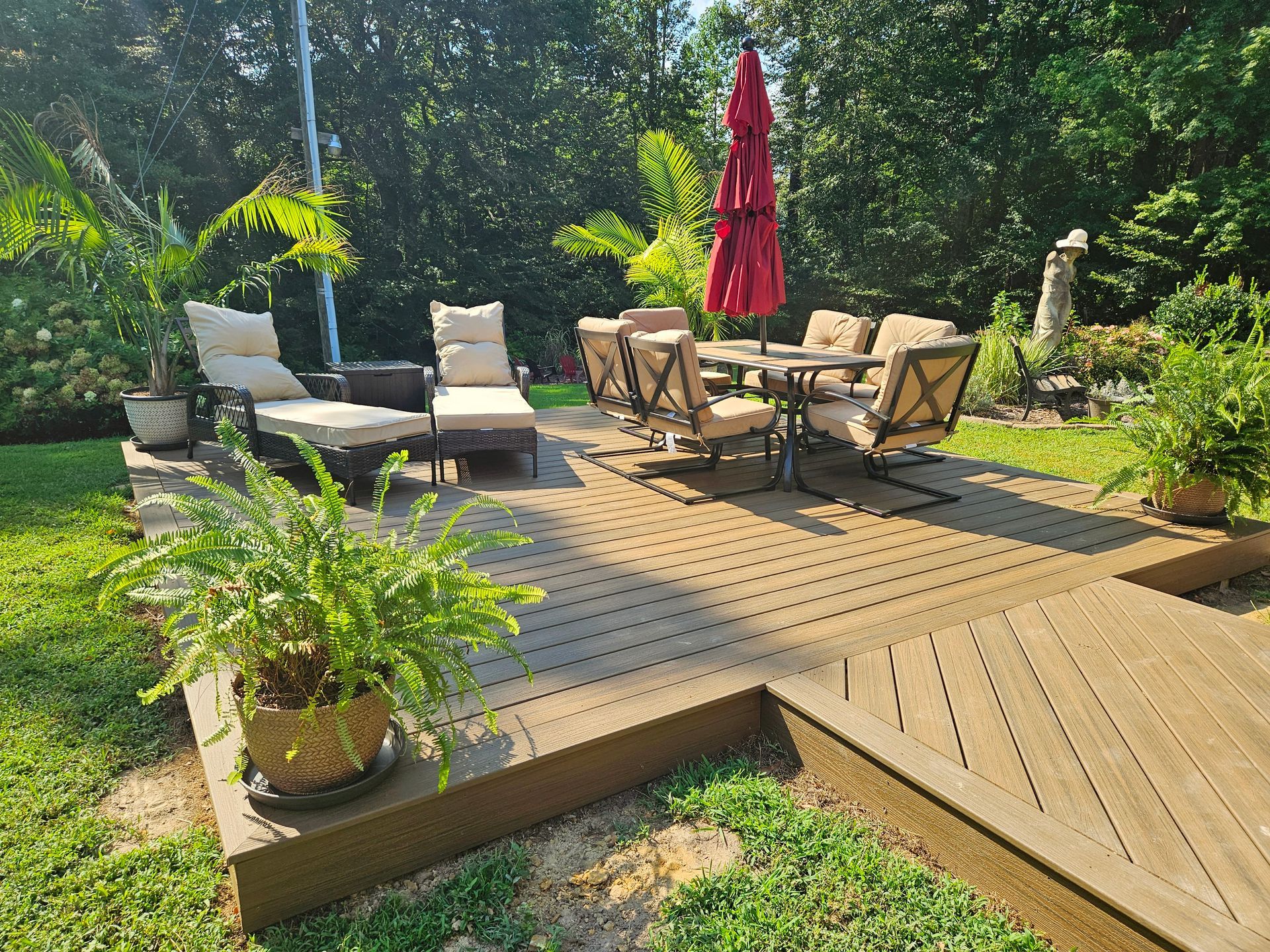 Backyard deck with patio chairs, table, red umbrella, and potted plants in sunlight