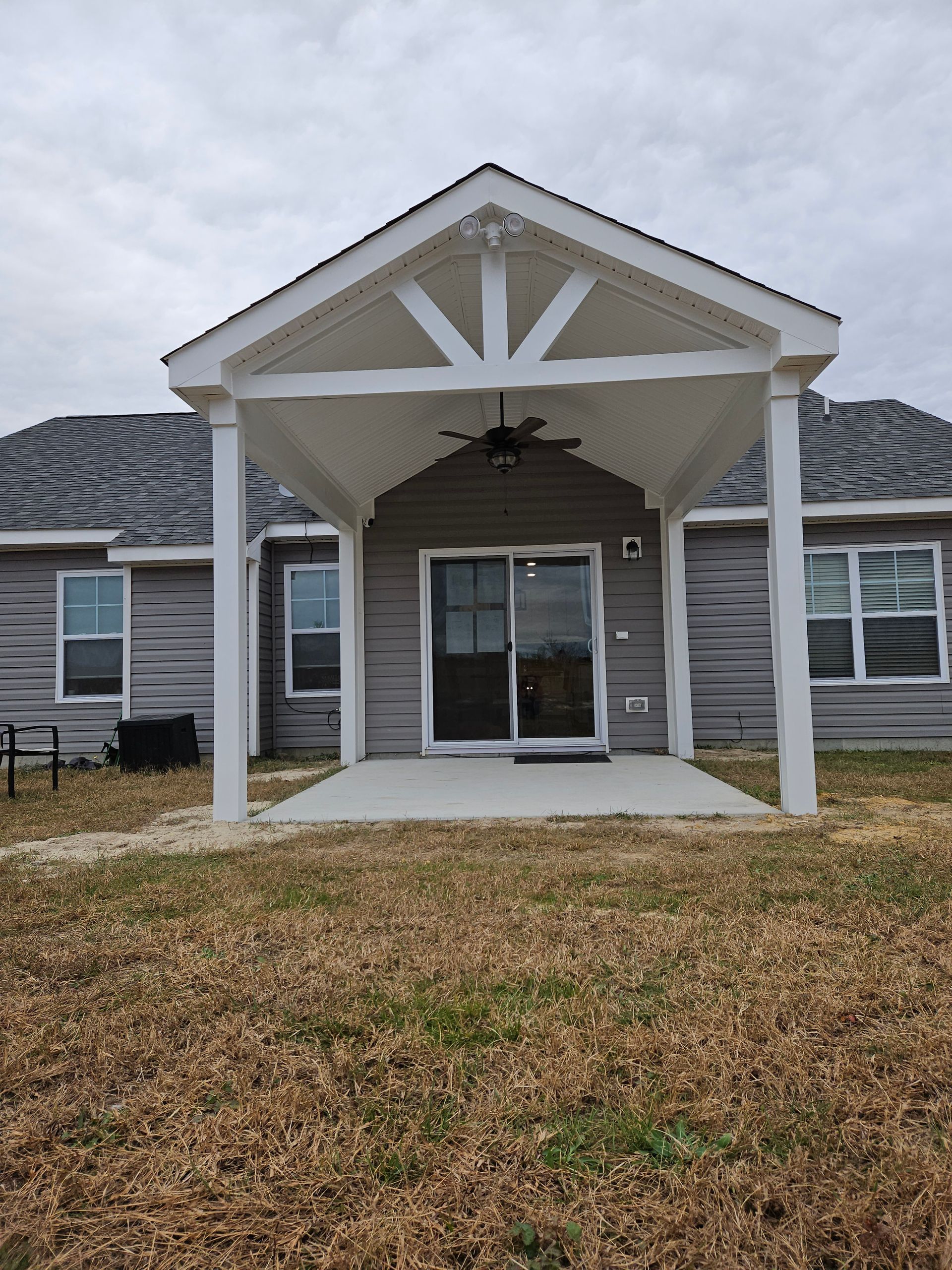 Front porch with white columns, sliding glass door, and a ceiling fan on a gray house.