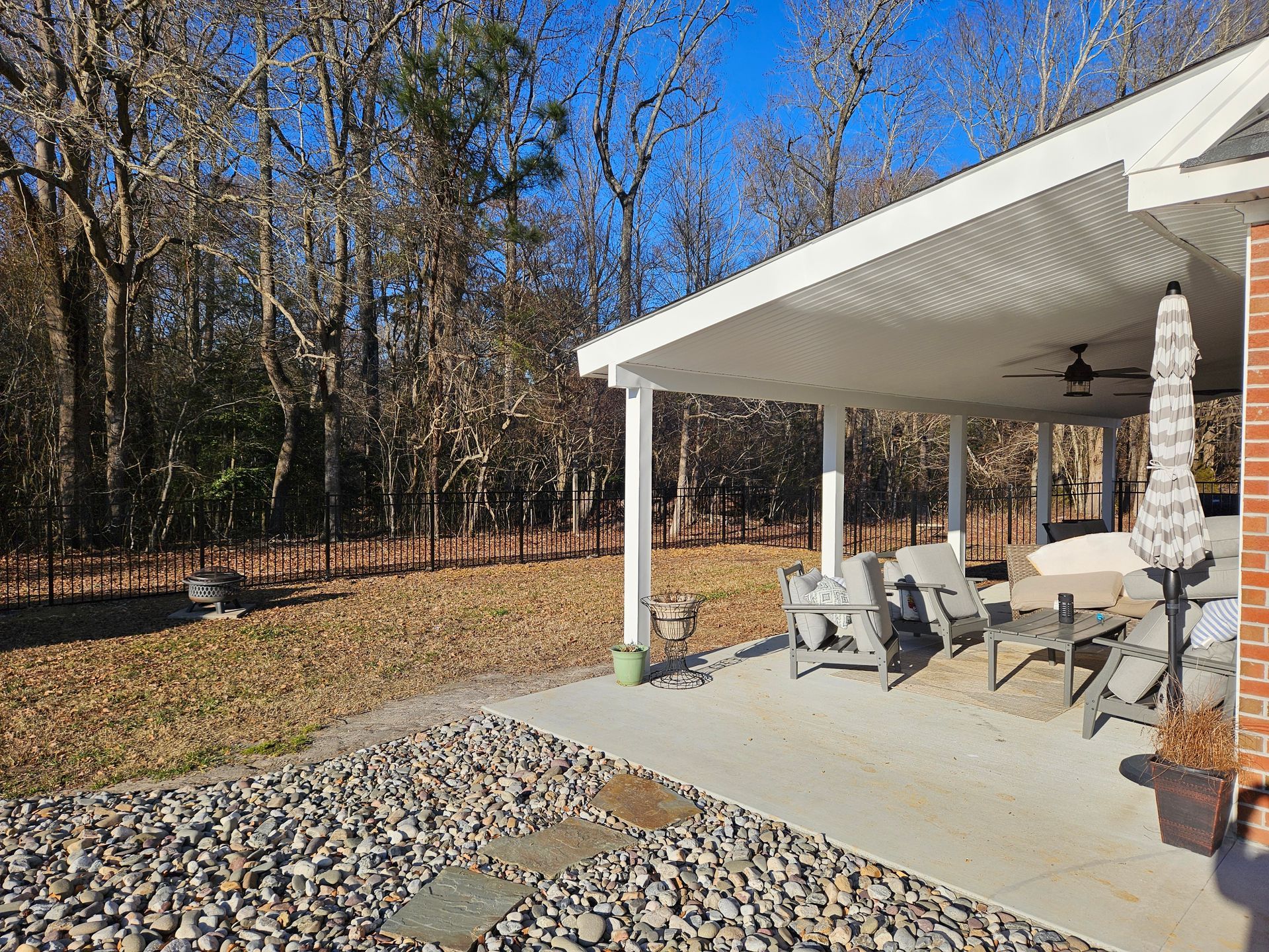 Covered patio with chairs and grill beside a wooded backyard on a sunny day