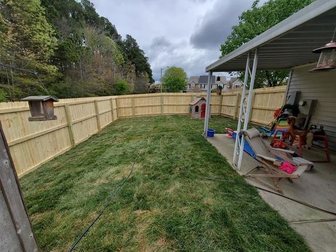 Backyard with fresh sod, wooden fence, and a covered patio with tools and a mower along the right side.