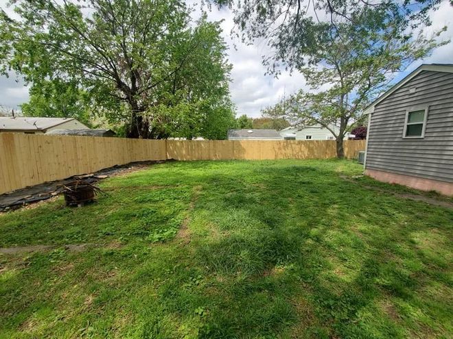 Backyard with green lawn, wooden fence, and a gray house under a partly cloudy sky